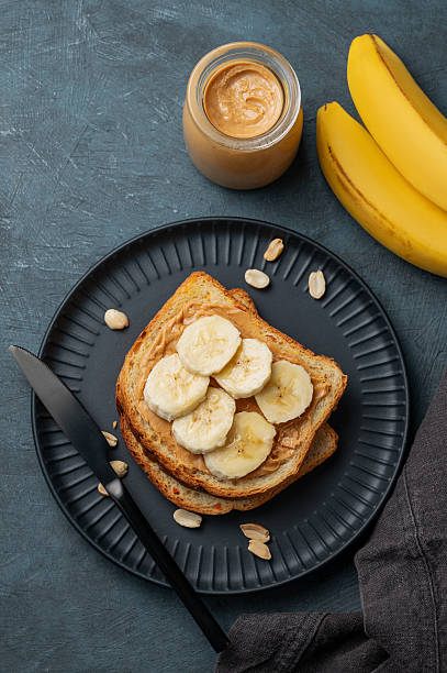 istock Peanut butter toast and banana on a black plate on a dark background with nuts 2247663748
