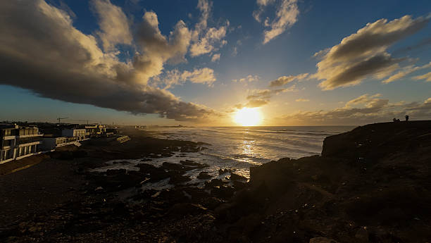 Sidi Ouassay, Chtouka Ait Baha - Morocco - 08-09-2024: Beach at sunset with people on sand and in water, golden light, scattered plastic chairs, and gentle waves in the sea.