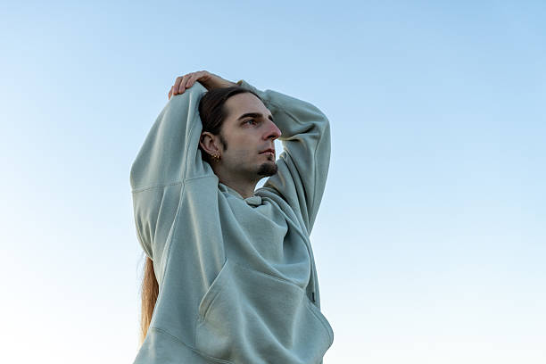 istock Young man with long hair stretching, wearing a hoodie while looking up, finding mindfulness and well-being 2247665277