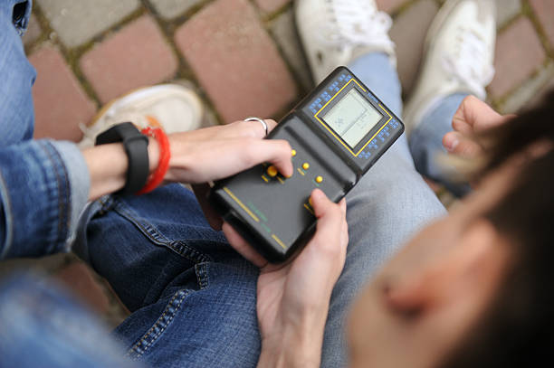 Young people engaged with a handheld device outdoors in a park setting.Technologies of the 90s.