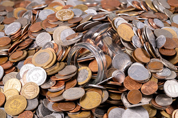 istock Collection of coins scattered around a glass jar on a table 2247666507