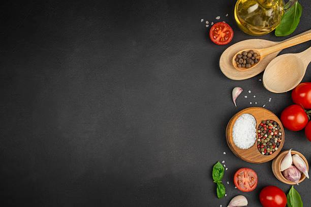 istock Fresh cooking ingredients on dark stone background with tomatoes, basil, garlic, spices, olive oil and wooden spoons arranged as a flat lay copy space recipe or food design projects 2247667186