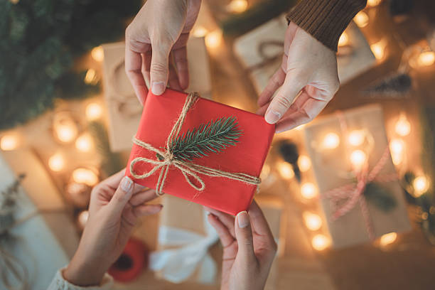 istock Christmas gift exchange with hands holding a beautifully wrapped red present decorated with natural twine and pine twig, symbolizing festive giving, warmth, celebration, and holiday tradition 2247667457