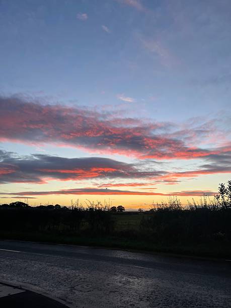 istock Dramatic Sunset Over Countryside Road - Vibrant sunset with dramatic clouds above a quiet rural road. 2247667637