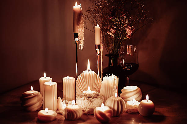 Close-up view of a festive table setting featuring a decorative candle holder on a reflective tray, with red chili peppers and citrus fruits arranged on a textured tablecloth, illuminated by warm indoor lighting.