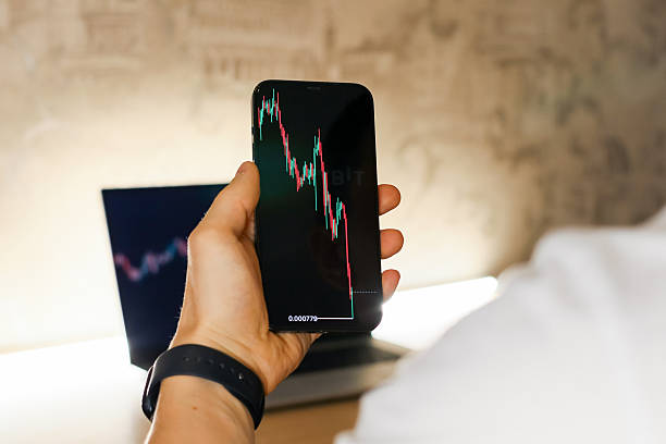 istock Hand holding smartphone displaying declining financial chart with laptop in background 2247672703