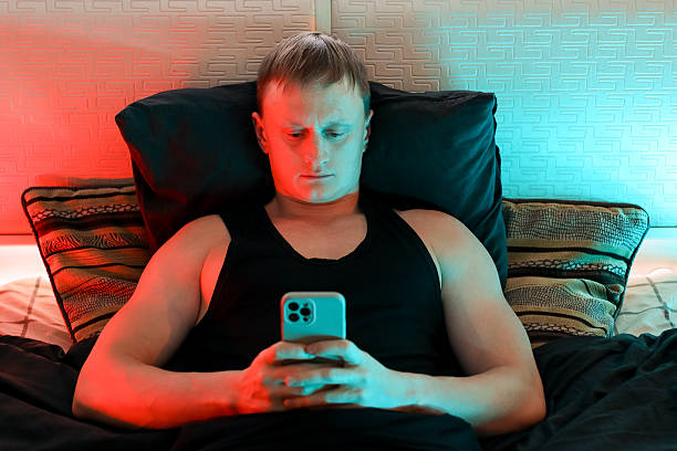 istock Young man in bed focused on smartphone under red and blue lights 2247672751