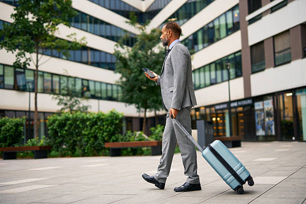 istock Businessman walking with suitcase checking phone in city 2247675975