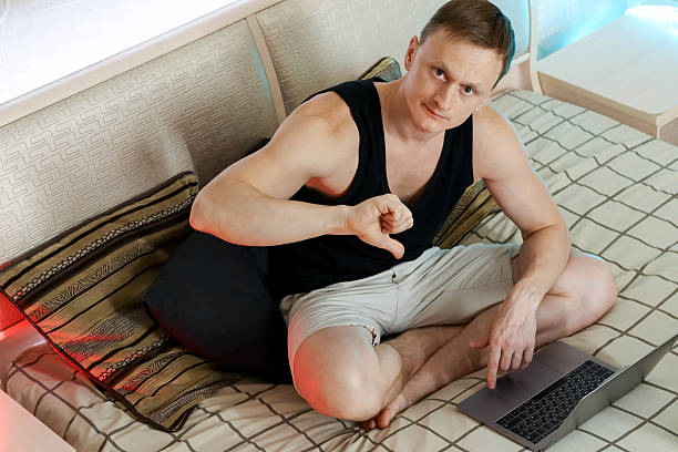 istock Man giving thumbs down gesture at laptop on comfortable bed 2247676018