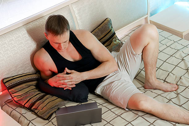Thoughtful man resting hands on lap beside laptop on comfortable bed