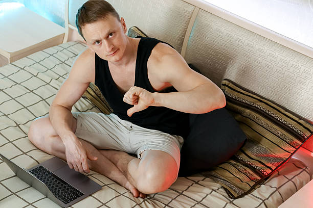 istock Disapproving young man with thumbs down near laptop on bed 2247676543