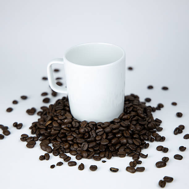 This visual presents a clean and modern still-life arrangement where a plain white mug stands at the center of a spread of rich roasted coffee beans. The composition emphasizes texture, contrast and simplicity, making it suitable for beverage-related branding, cafe promotions or editorial content. The neutral studio background highlights the shapes and tones of the beans, while the uncluttered setup supports themes of morning rituals, specialty coffee culture and product identity.