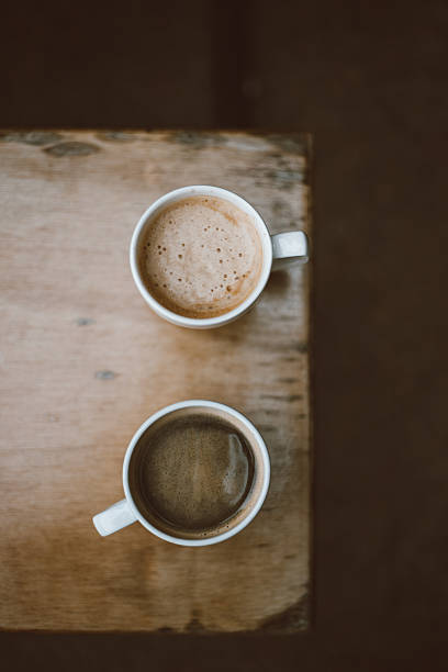 Top view of two ceramic coffee cups with different brews on rustic wooden surface, Warm tones and natural textures in cozy café setting, Beverage concept for menu design and lifestyle visuals