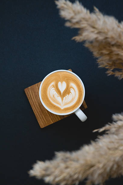 Top view of a latte with heart-shaped latte art placed on wooden coaster against dark background, Warm tones and modern café aesthetic, Specialty coffee concept for menu and branding visuals