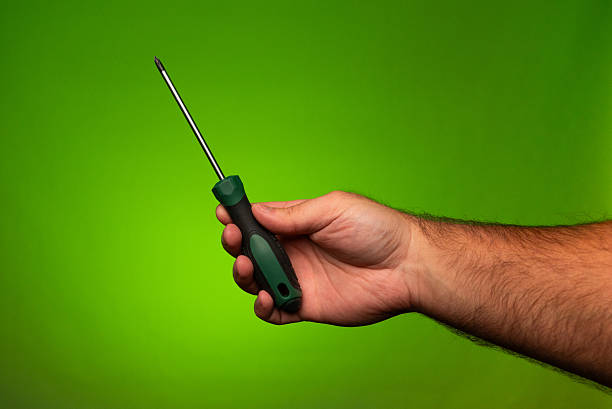 A man holding a green Philips head screwdriver in his hand. Man holding a Philips screwdriver. Green Philips screwdriver