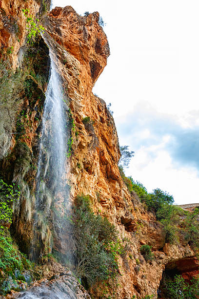 istock Majestic Waterfall Cascading Down Rocky Cliffs, Surrounded by Lush Greenery Under a Cloudy Sky 2247681096