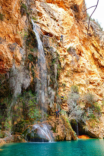 A group of thrill-seekers descends a steep waterfall, surrounded by vibrant rock formations and greenery.