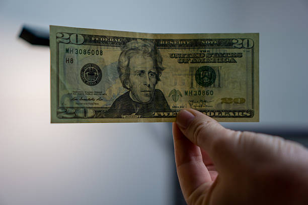 istock hand holding a twenty dollar bill up to the light, single currency note held for close up inspection, checking for security features and authenticity, concept of financial security, fraud detection 2247683759