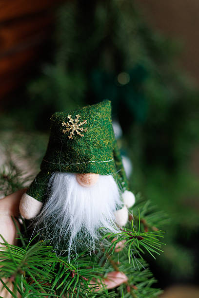 Authentic handmade gnome ornament with warm home crafted details on fir branches in a green and gold palette.Concept of cozy holiday decoration, greeting card, banner and rustic seasonal marketing.