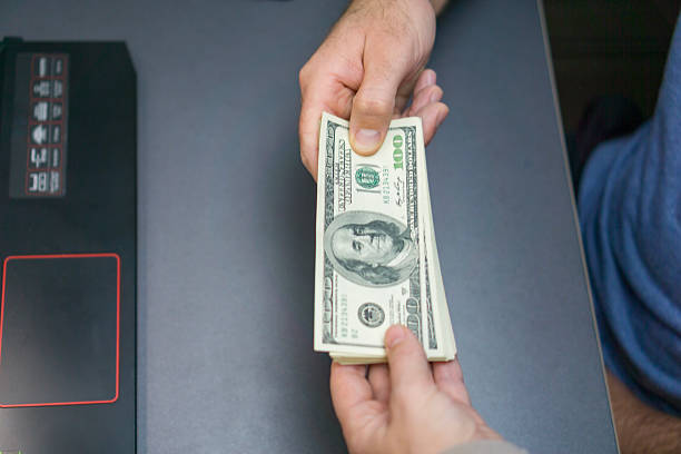 istock two hands exchanging a large stack of one hundred dollar bills across a dark desk next to a laptop, concept of financial exchange, business investment, bribery or loan 2247684225