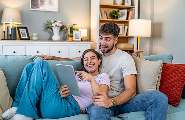 istock Young couple laughing enjoying tablet content on sofa 2247684900