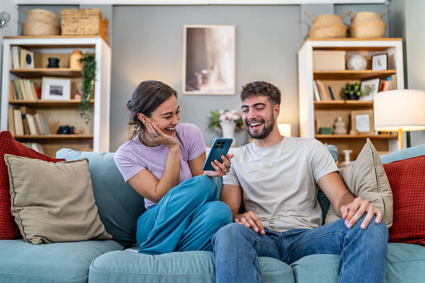 istock Young couple laughing using smartphone on couch at home 2247686201