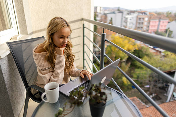 istock Beautiful woman sitting on her balcony and working on her laptop 2247686332