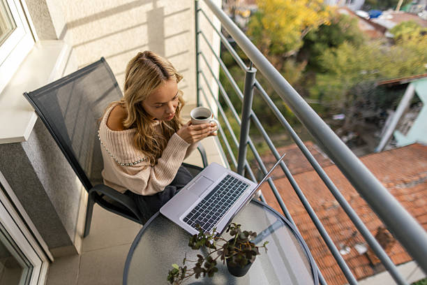 istock Beautiful woman sitting on her balcony and working on her laptop 2247686349