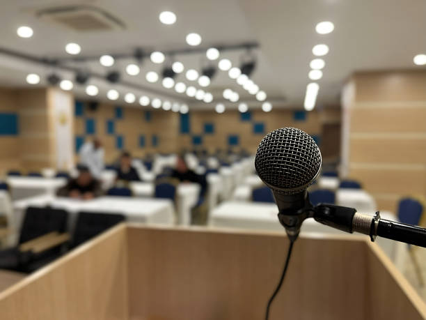 istock A microphone on a podium and a conference hall waiting in the blurred background. Presentation, speech, and event themes. 2247688749