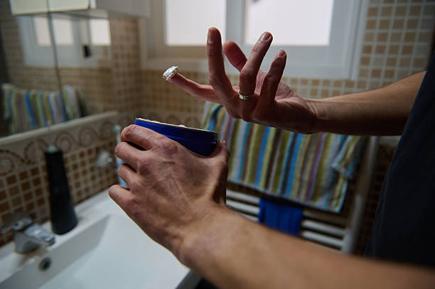 A man at home in a bathroom applies a small bandage to his injured finger, gripping a mug. The scene captures everyday life, care, and casual home routine.