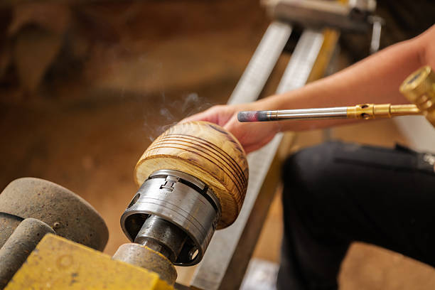 istock Carpenter burning a wooden object attached to a lathe machine, using a small torch in a dusty old workshop, showcasing skillful craftsmanship and dedication to the art of woodworking 2247692970