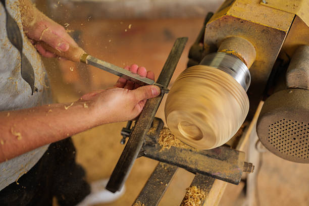 Carpenter meticulously shapes a wooden bowl on a lathe, using a chisel with precision, amidst swirling wood shavings in a traditional workshop, showcasing craftsmanship and woodworking skills