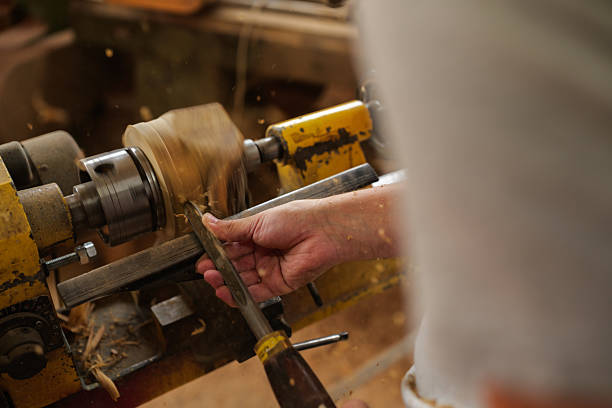 Carpenter's hands skillfully working wood on a lathe, shaping a raw piece of timber while sawdust swirls around the workshop, highlighting the artistry of woodworking