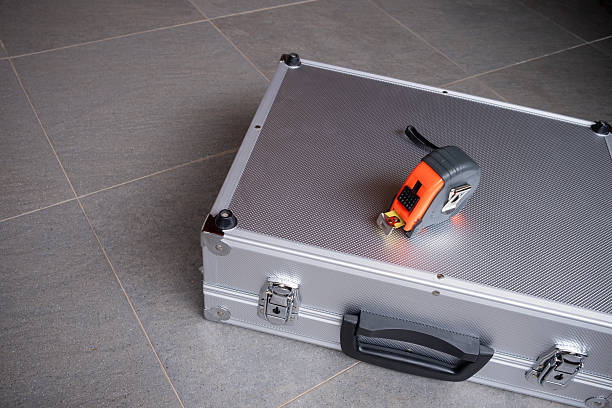 A tape measure rests on a metallic tool briefcase set on a gray tiled floor, construction, home improvement, professional tools, and precision with ample copy space, horizontal