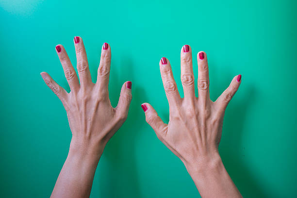 Female hands with red nails on a green background. Top view.