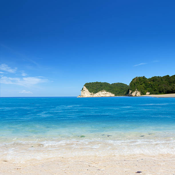 istock Beautiful tropical beach with turquoise water, sand, and lush green cliffs under a blue sky background. Natural background 2247721866