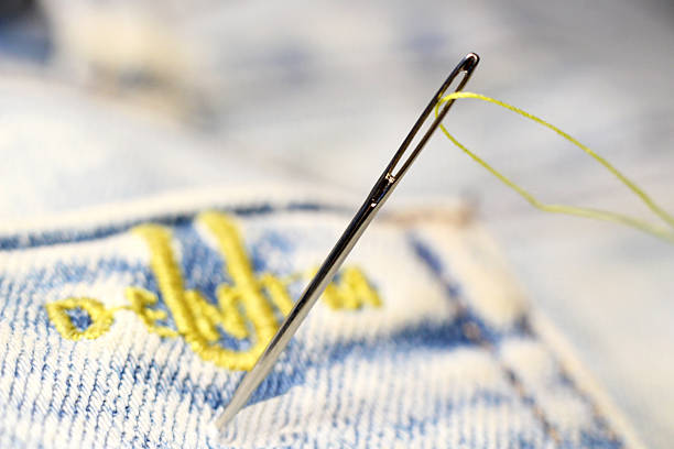 A sewing needle and yellow embroidery on jeans, sewing industry. Macro.
