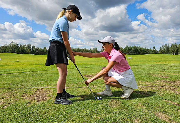 Golf coach instructs young girl on driving technique during sunny day at driving range in summer