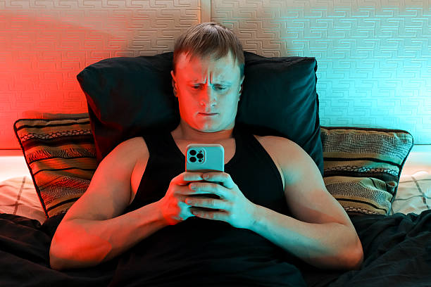 istock Frowning man in bed scrolling smartphone amid neon glow 2247732658