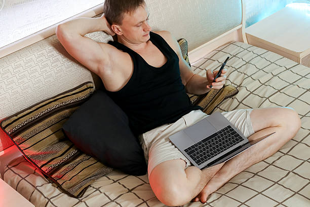 istock Man holding phone thoughtfully with laptop on bed 2247732723