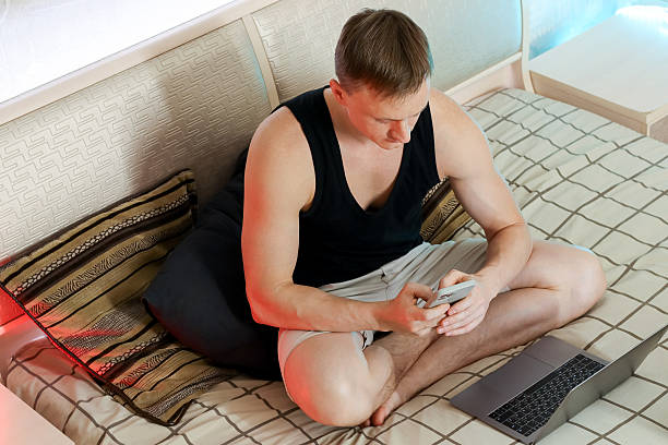 istock Young man checking smartphone beside laptop on cozy bed 2247732945