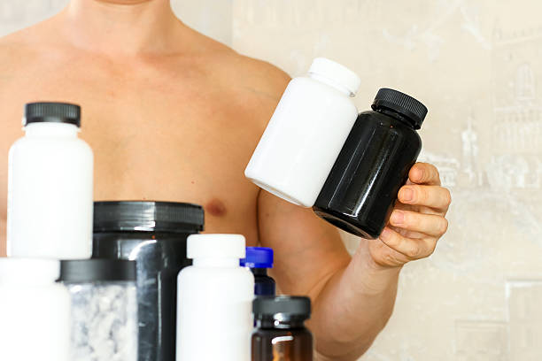 istock Muscular man holding two supplement bottles among many 2247736637