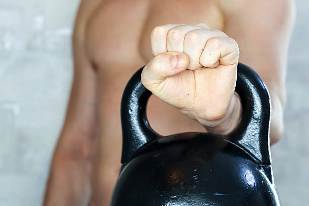 Strong muscular man gripping kettlebell handle with closed fist. Close-up of powerful male fist tightly holding black kettlebell, showing strength and determination