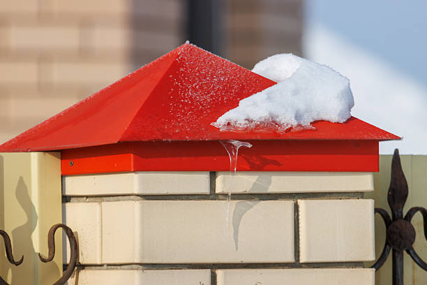 A red roof with snow on it. The snow is melting and dripping down the roof. The roof is on a brick wall