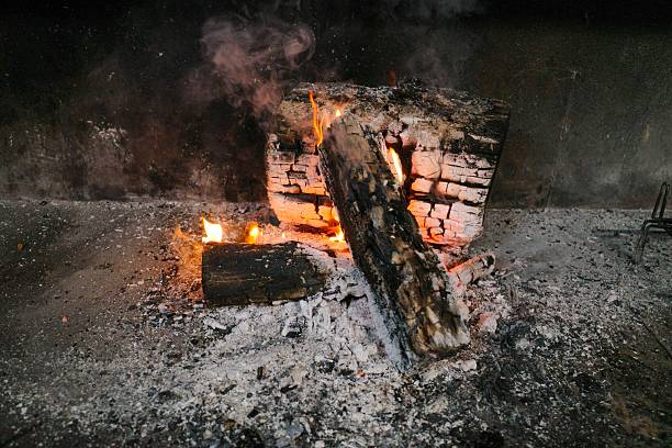 Burning wood slowly in a fire to prepare embers for cooking