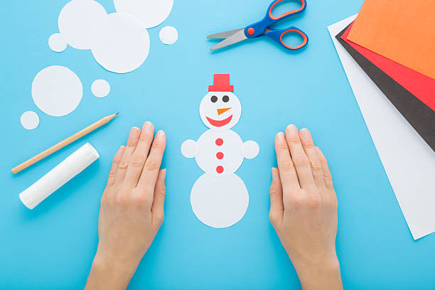 istock Young woman hands creating and decorating snowman shape from white paper. Light blue table background. Pastel color. Making winter element for little child. Closeup. Point of view shot. Top down view. 2247748321