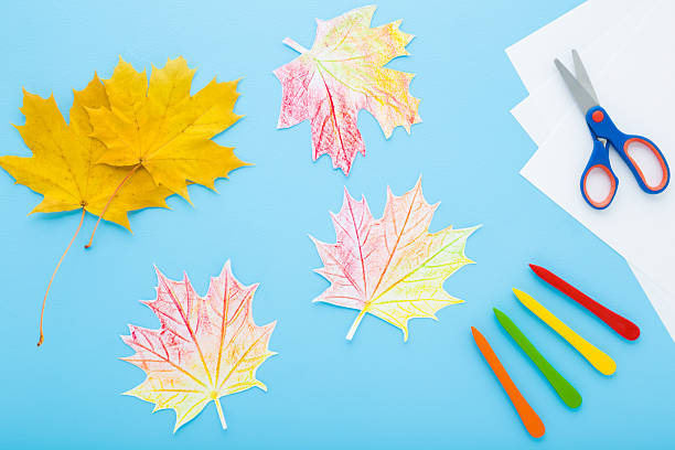 istock Painting and copying colorful maple leaf pattern. Wax crayons, white paper, scissors on light blue table background. Pastel color. Little child handcraft. Closeup. Top down view. 2247748349