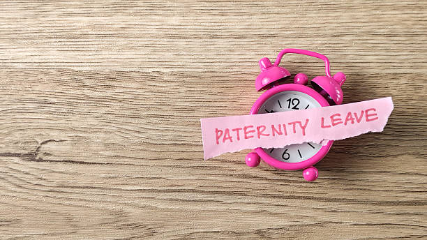istock Paternity Leave concept with a pink sticky note wrapped around a small alarm clock on a wooden desk, symbolizing time management and family responsibility. 2247753287