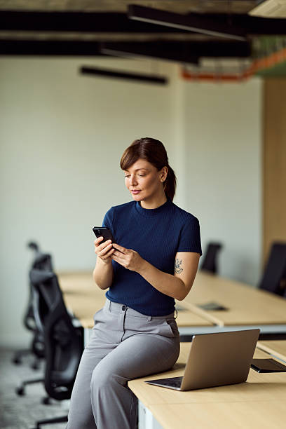 istock Professional Woman Using Smartphone In Modern Office With Laptop On Desk And Minimalist Design 2247753509