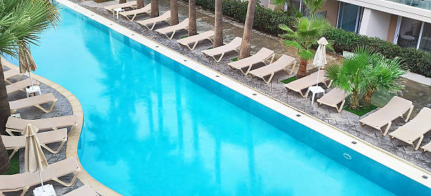 Swimming pool with chairs for tanning near blue fresh water. Palms reflected in the water. Summer, vacation, resort, relaxation, sport concept.